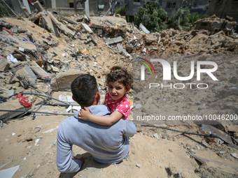 Palestinian man with his daughter sits amidst the rubble of his house in Gaza City, on May 15, 2023, following a ceasefire ending five days...
