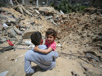 Palestinian man with his daughter sits amidst the rubble of his house in Gaza City, on May 15, 2023, following a ceasefire ending five days...