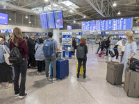 Passenger holding baggage are seen walking in front of the departure screen board and the check-in counters, pulling their luggage. People w...
