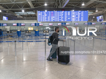 Passenger holding baggage are seen walking in front of the departure screen board and the check-in counters, pulling their luggage. People w...