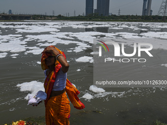 A woman stands on the banks of river Yamuna covered with toxic foam caused by industrial discharge, on the World Environment Day, in New Del...