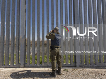Police officer searches the area for people with binoculars. Greek border police officers patrol along the steel fence next to Evros river b...