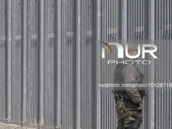 Border police officers stands in front of the fence searching for illegal entry. Greek border police officers patrol along the steel fence n...