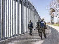 Border police walking alongside the fortification fence with a watch tower post in the background for police and the military equipped with...