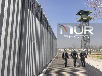 Border police walking alongside the fortification fence with a watch tower post in the background for police and the military equipped with...