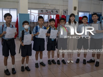 Students holding their secondary school allocation result posing for a photo with their teacher at a school hall on July 11, 2023 in Hong Ko...