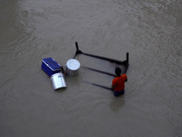 A man carries his belongings as he wades through the flooded waters in a low-lying area, after being displaced by the rising water level of...