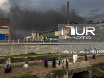 People are walking past an iron industry that is emitting toxic smoke into the air in the early morning in Dhaka, Bangladesh, on December 4,...