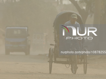 A rickshaw and a commuter are seen on a dusty and heavily polluted road in Dhaka, Bangladesh, in December 2023. (