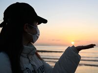 A tourist is holding the New Year sunrise with his palm during a photo shoot at the Golden Beach in Qingdao, China, on January 1, 2024. (