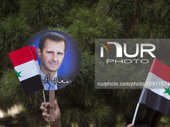 A supporter of Syria's President Bashar al-Assad is holding up a flag and a portrait of Bashar al-Assad during the 2014 Syrian Presidential...