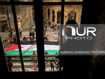 A woman is watching from a window as protesters are carrying a big Palestinian flag in support of Palestine and against the Israeli governme...