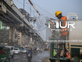 A worker is spraying water from a truck to control dust in a polluted area in Dhaka, Bangladesh, on January 19, 2024. (