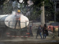 A worker is spraying water from a truck to control dust in a polluted area in Dhaka, Bangladesh, on January 19, 2024. (
