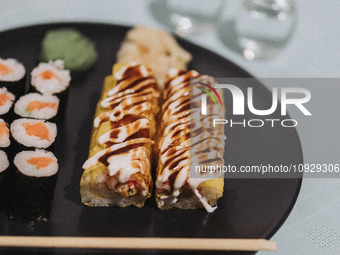 Banana sushi rolls and salmon maki sushi rolls are sitting on a plate next to two glasses of sake in Athens, Greece, on January 21, 2024. (