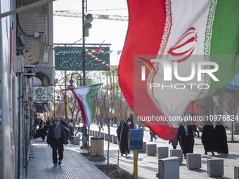 People are walking past Iranian flags hanging on a sidewalk in the holy city of Qom, 145 km (90 miles) south of Tehran, on February 7, 2024....