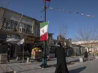 A veiled Iranian woman is walking past an Iranian flag that is hanging on a sidewalk in the holy city of Qom, 145 km (90 miles) south of Teh...