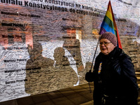 Women rights activist from the Women's Hell organisation  holds a rainbow flag and walks in front of a giant banner calling President Andrze...