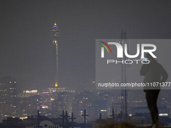 A young Iranian man is using his cellphone with a view of the Milad telecommunications tower in the background in northwestern Tehran, Iran,...