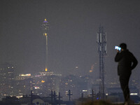 A young Iranian man is using his cellphone with a view of the Milad telecommunications tower in the background in northwestern Tehran, Iran,...
