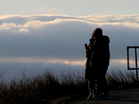 A couple is looking at photos on their mobile device as the sun sets and clouds form at the Final Approach Danville Terminal, an aviation-th...