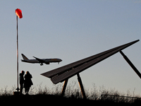 A couple is watching a plane arrive at Toronto Pearson International Airport while the sun sets at the Final Approach Danville Terminal, an...
