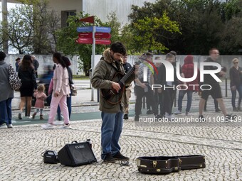 People are walking near a man who is playing a guitar along one of the walkways in Das Nacoes Park in the Oriente district, in Lisbon, Portu...