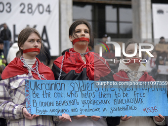 Three women are standing with their mouths covered with red ribbons during the ''Don't Keep Silent! Captivity Kills!'' action in support of...