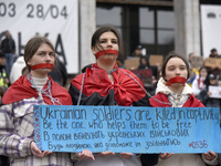 Three women are standing with their mouths covered with red ribbons during the ''Don't Keep Silent! Captivity Kills!'' action in support of...