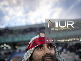A man is wearing a Palestinian scarf and holding a portrait of Iran's Supreme Leader Ayatollah Ali Khamenei while participating in a religio...