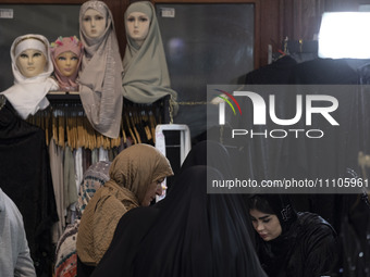 Veiled Iranian women are standing together under mannequins covered with mandatory headscarves during the Hijab and Chastity fair at the Ima...