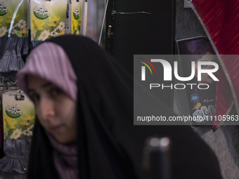 A veiled Iranian woman is standing next to a portrait of a female Iranian-Islamic fashion model while visiting the Hijab and Chastity fair a...