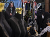 A veiled Iranian woman and her young daughter are looking at dresses next to a poster featuring a portrait of a female Iranian-Islamic fashi...