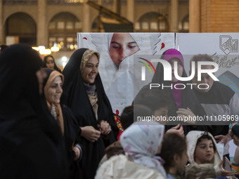 Veiled Iranian women are standing in front of a banner featuring a portrait of a young Iranian veiled girl during the Hijab and Chastity fai...