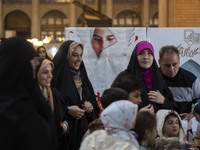 Veiled Iranian women are standing in front of a banner featuring a portrait of a young Iranian veiled girl during the Hijab and Chastity fai...
