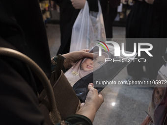 A veiled Iranian woman is looking at a portrait of a female Iranian-Islamic fashion model while shopping at the Hijab and Chastity fair in t...