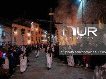 People wearing white hooded costumes and bringing Jesus Christ cross are seen next to a giant fire during Good Friday procession in Gubbio,...