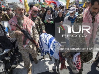 Armed military personnel from the Islamic Revolutionary Guard Corps (IRGC) are walking alongside a donkey draped with an Israeli flag and we...