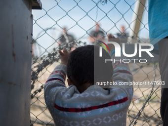 Child touching the fence of the Macedonian border. Macedonian police behind it. In Idomeni camp on April 6, 2016. (