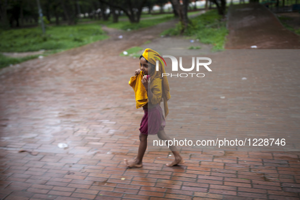 A homeless child walking in a park cover her head with a yellow cloth to save from rain water in Dhaka, Bangladesh on May 24, 2016. 