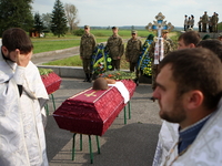 Ukrainian servicemen with an Orthodox priest stand next to coffins during a mass funeral ceremony in front of the memorial for the defenders...