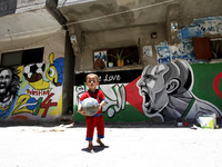 A Palestinian boy carrying the flag of the Algerian a in front of graffiti wall murals depicting football players the participants at 2014 W...