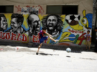 A Palestinian boys play a ball in front of graffiti wall murals depicting football players the participants at 2014 World Cup Brazil (LtoR)...