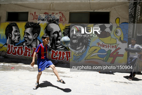 A Palestinian boys play a ball in front of graffiti wall murals depicting football players the participants at 2014 World Cup Brazil (LtoR)...