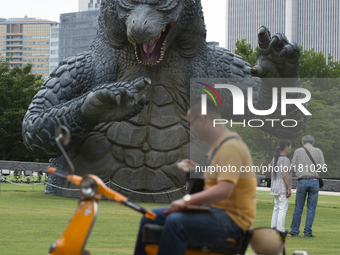 A man sits on his scooter with a Godzilla statue beside him. The 6.6 meters statue of godzilla is displayed in Midtown Park in Tokyo to prom...