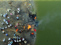 Indian hindu people gather near a dead body of their relative as they prepare to cremate on the polluted banks of Ganges river , in Allahaba...