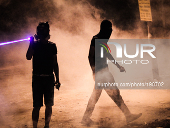 Bahrain , Abu Saiba - (R) protester walking in tear gas clouds while other protester using a lazer on riot police (L) , demonstration follow...