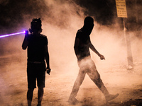 Bahrain , Abu Saiba - (R) protester walking in tear gas clouds while other protester using a lazer on riot police (L) , demonstration follow...
