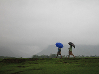 Bangladeshi men hold umbrellas to protect themselves from rain walk alone a river side during the rainy day at Bisanakandi in Sylhet, Bangla...