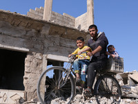 A Syrian man rides a bike carryin his children past  destroyed buildings in the rebel-held town of Douma, on the eastern outskirts of the Sy...